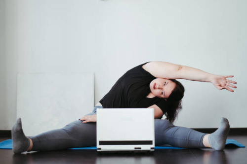 Woman doing a straddle stretch at home with her laptop
